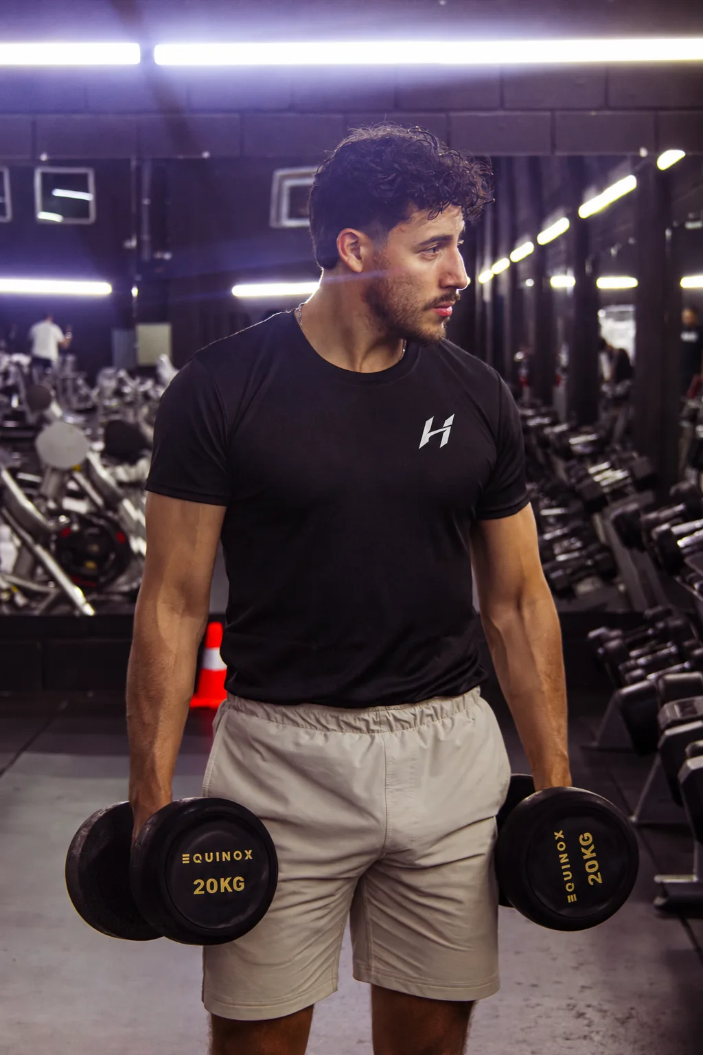 Atleta Hustform con camiseta negra de pie en el gimnasio, mirando hacia un lado